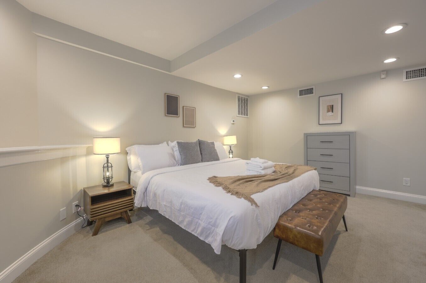 A bedroom with a bed, bedside tables, a bench, and a dresser.