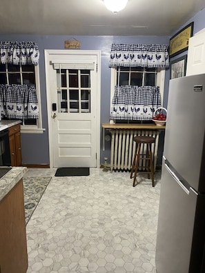 A kitchen with a white door, checkered curtains, a radiator, a wooden stool, and a refrigerator. - Historic Springdale Mill Farmhouse with Spa House (Winchester)
