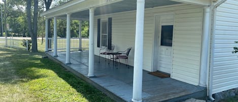 A white house with a covered porch, numbered 115, featuring a small table and chairs.