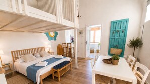 A bedroom with a bed, bedside tables, a bench, a dining table with chairs, and a blue door. - Vrbo Property (Bacoli)