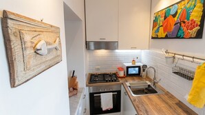 A compact kitchen with white cabinets, a gas stove, a microwave, and a sink. - Vrbo Property (Bacoli)
