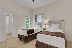 Ein Hotelzimmer mit zwei Betten, einem Fenster mit Jalousien, einer Tür und einem Nachttisch mit Lampe.