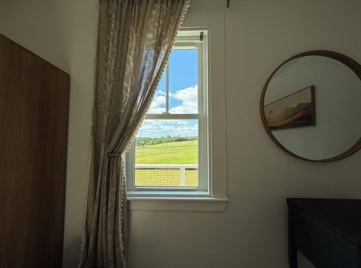 A room with a window, a painting on the wall, and a dark piece of furniture.