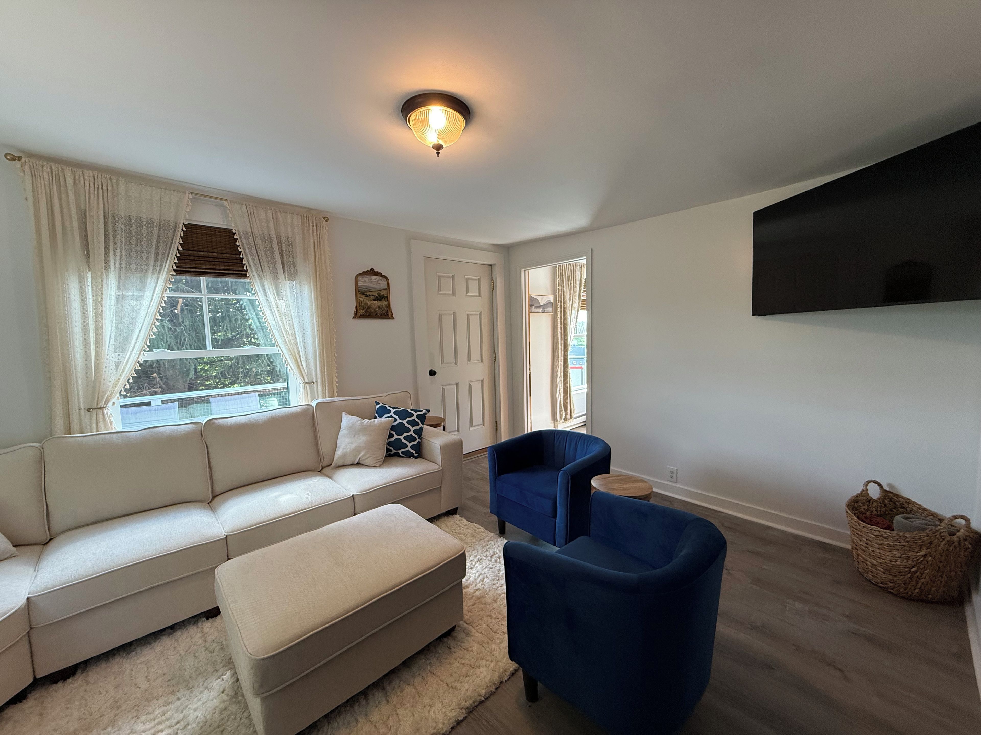 A living room with a sofa, ottoman, blue armchair, and a flat-screen TV mounted on the wall.