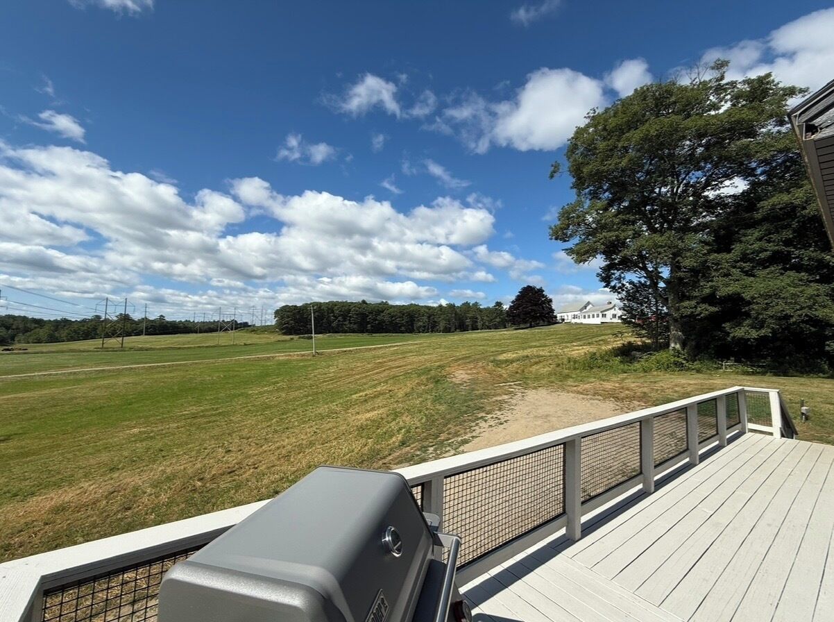 A deck with a grill, overlooking a grassy field and a building in the distance.