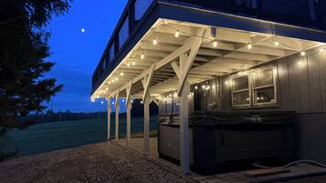 A covered outdoor area with a barbecue grill, string lights, and a view of a building with a metal roof.