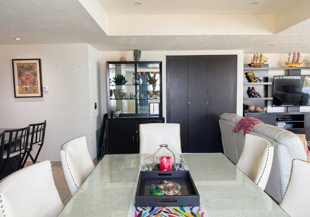 A dining area with a table, chairs, a cabinet with glass doors, and a TV in the background.