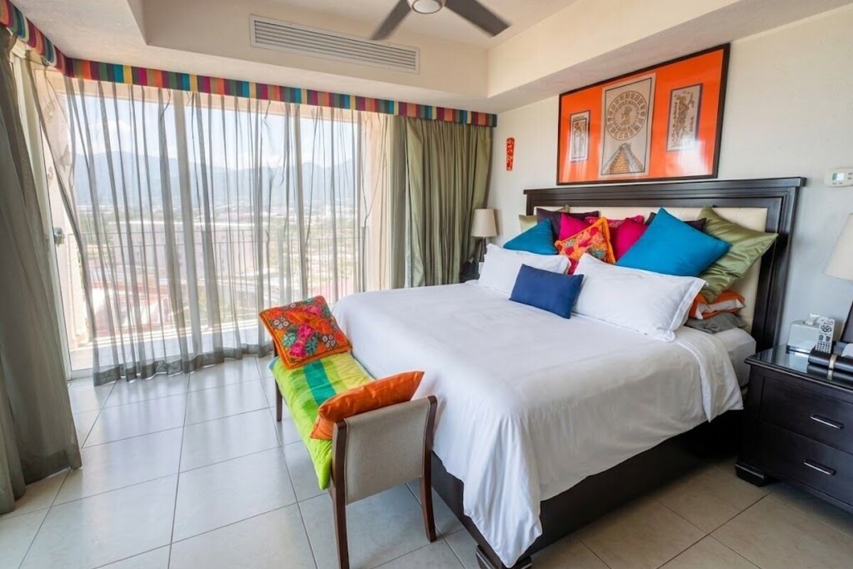 A hotel room with a bed, a chair, a bedside table, a lamp, and a window with curtains.