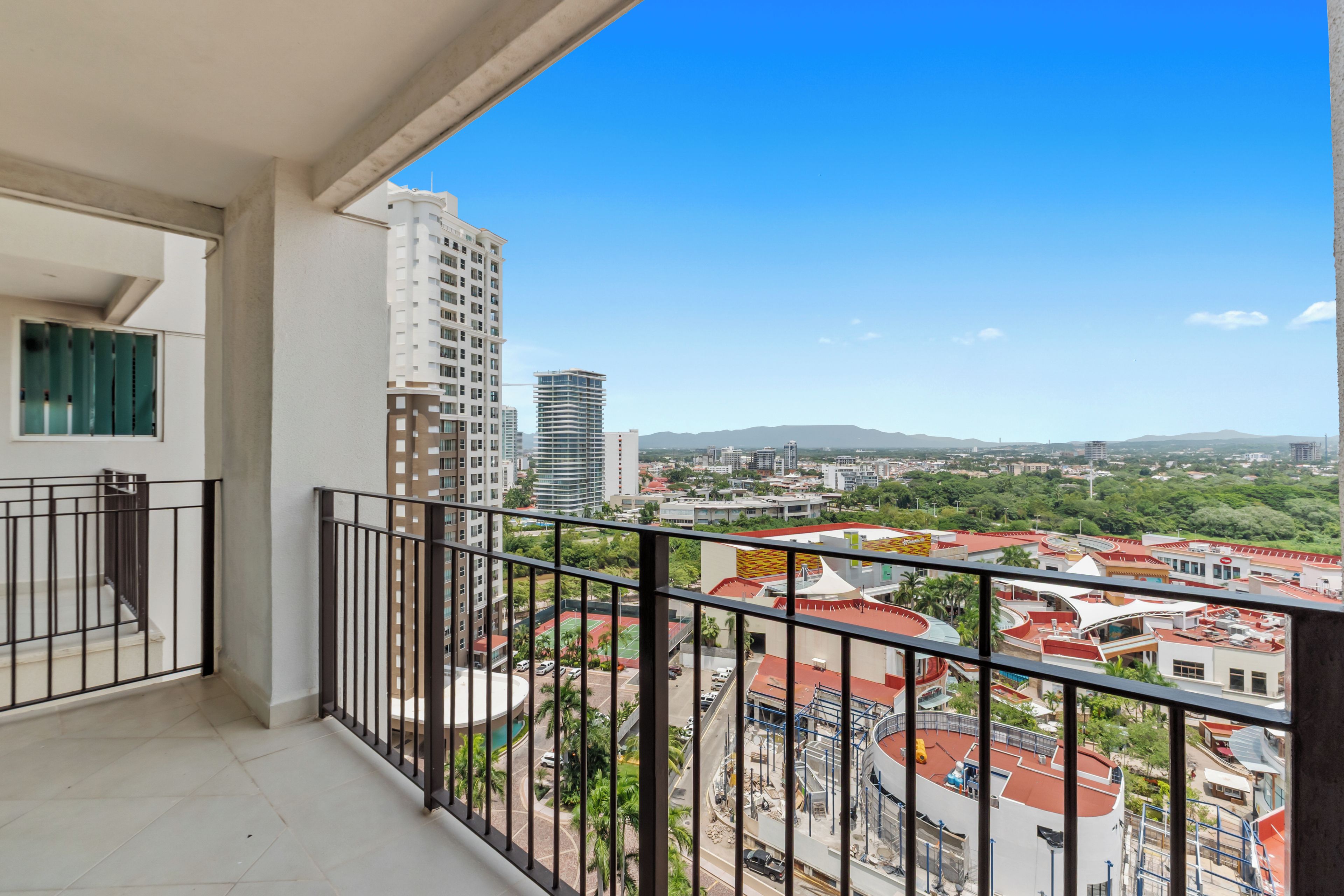 A balcony with a view of a cityscape, including buildings and greenery.