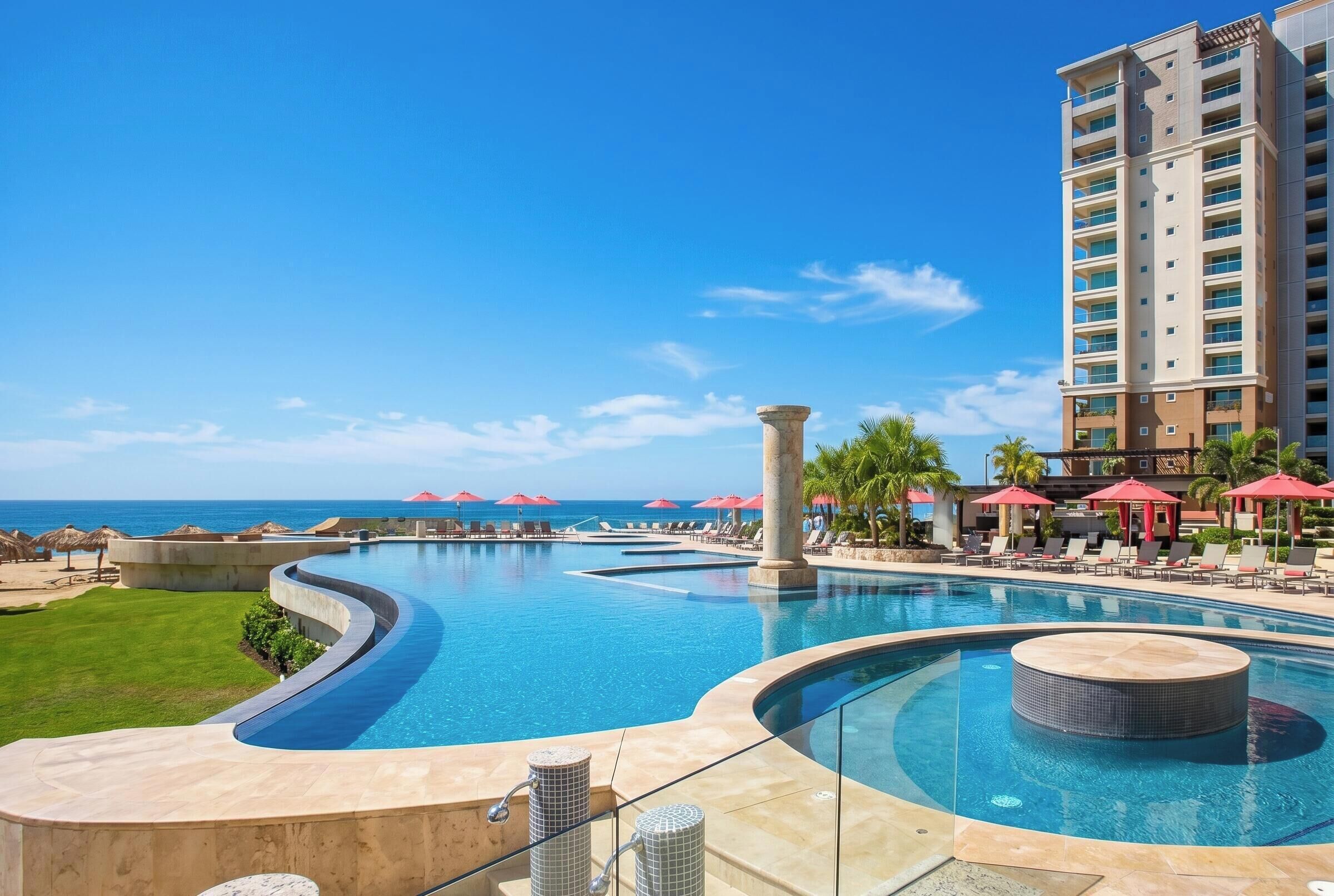 A resort pool with a curved design, a hot tub, and lounge chairs with umbrellas.