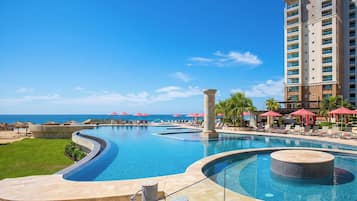 Una piscina de diseño curvo en un complejo turístico, con un jacuzzi y sillones de descanso con sombrillas.