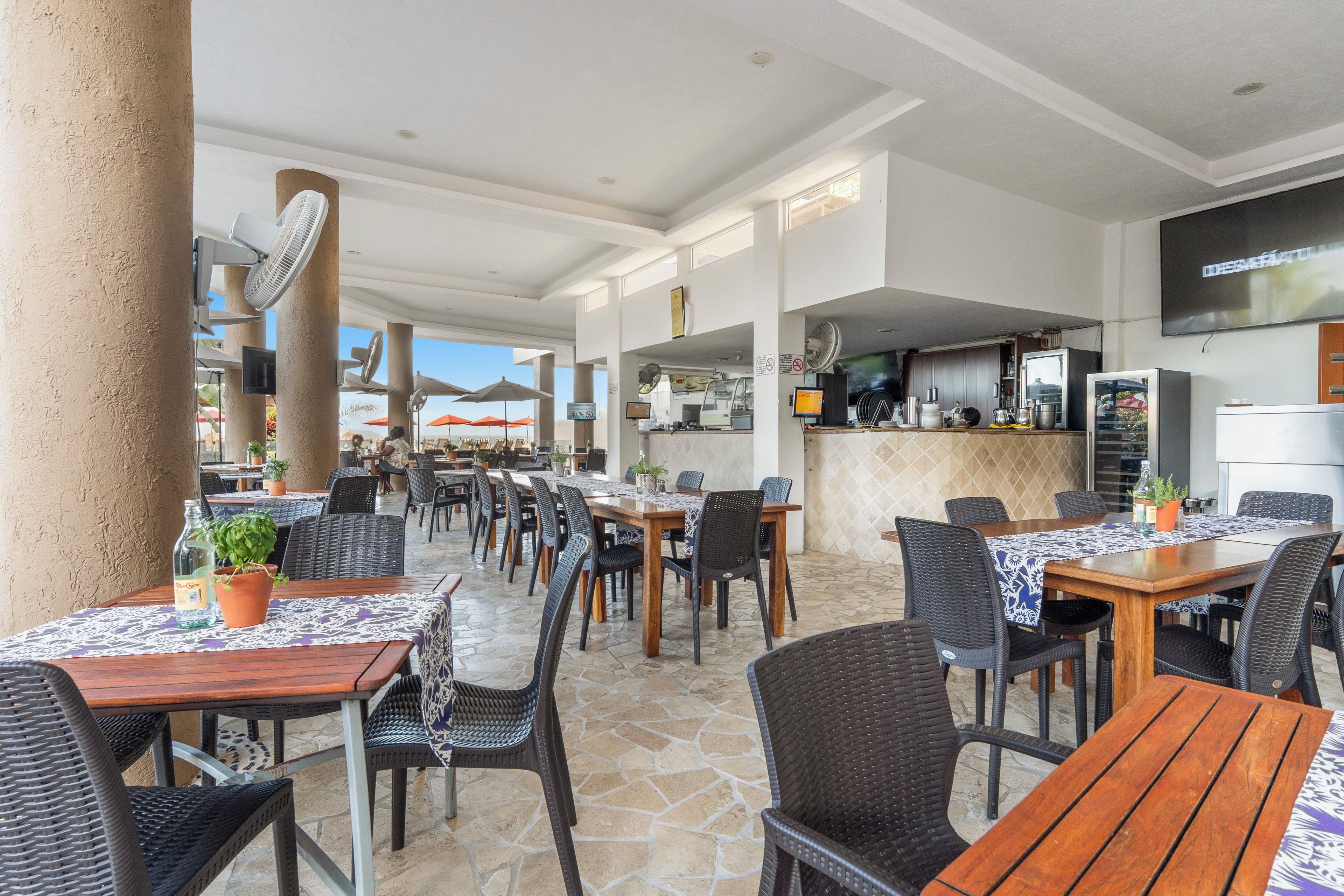 An outdoor dining area with tables and chairs, a bar area, and a television screen on the wall.