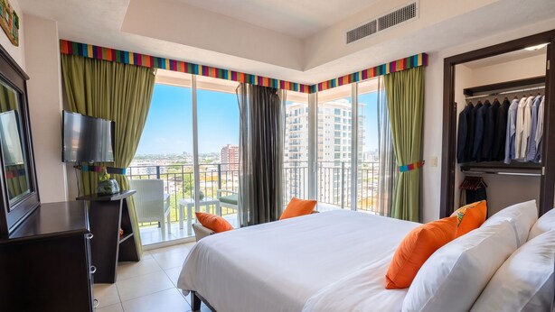 Una habitación de hotel con cama, televisión, armario y balcón con vistas a la ciudad.