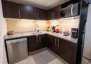 A modern kitchen with dark wood cabinets, stainless steel appliances, and a granite countertop. - Grand Venetian Oceanfront by Monyxbnb (Puerto Vallarta)