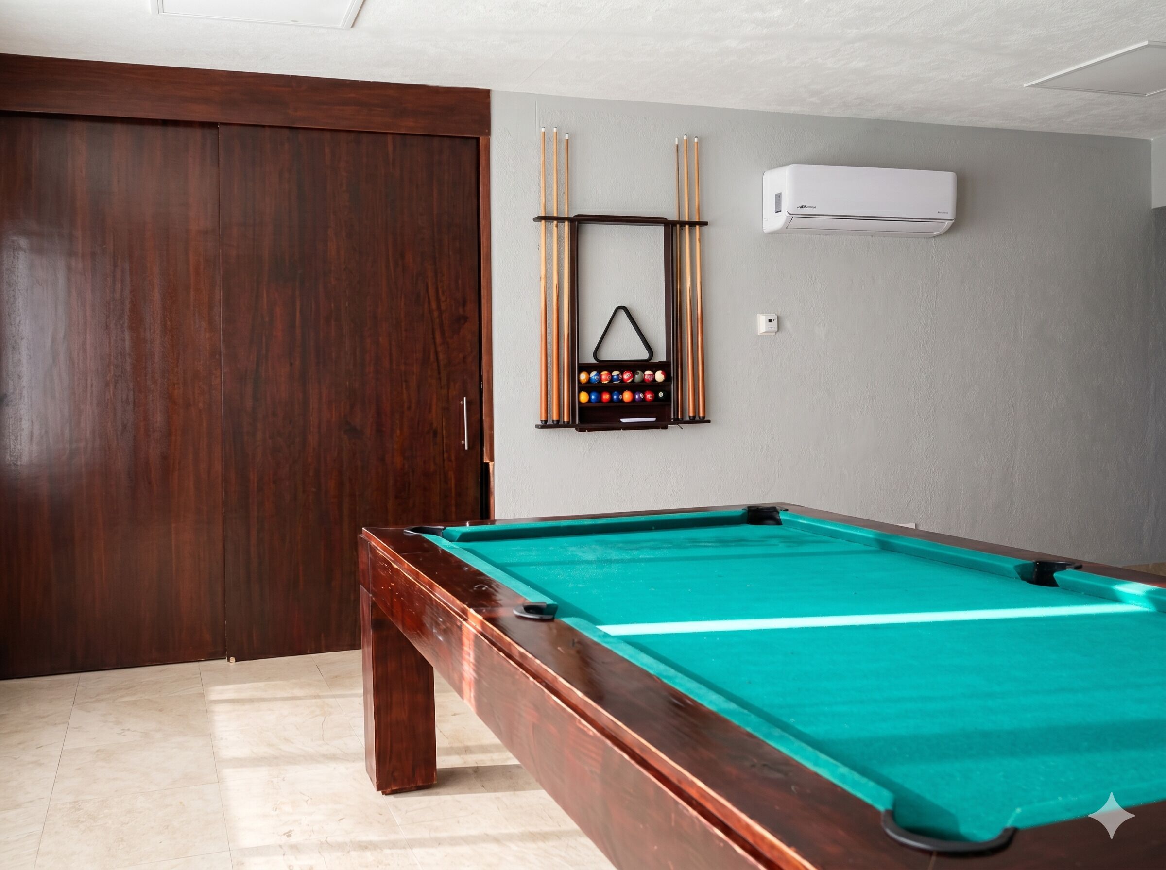 A pool table with a green felt surface, a wooden pool table frame, and a cue rack with pool cues and balls.