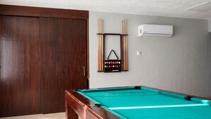 Una mesa de billar con superficie de fieltro verde, estructura de madera y un atril para tacos con tacos y bolas.