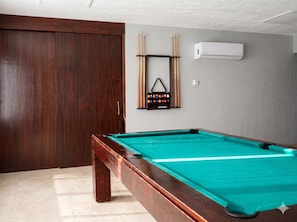 A pool table with a green felt surface, a wooden pool table frame, and a cue rack with pool cues and balls. - Grand Venetian Oceanfront by Monyxbnb (Puerto Vallarta)
