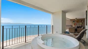 A balcony with a view of the sea, a hot tub, and a seating area with a table and chairs.