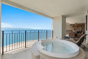 Ein Balkon mit Meerblick, einer Whirlwanne und einer Sitzecke mit Tisch und Stühlen.