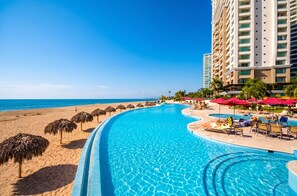 A resort pool with a beach view, palm trees, and a high-rise building. - Grand Venetian Oceanfront by Monyxbnb (Puerto Vallarta)