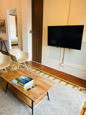 A modern living room with a flat-screen TV, a coffee table with books and a remote, two white chairs, and a patterned rug. - La Botica, Casa Donovan (Panamá)