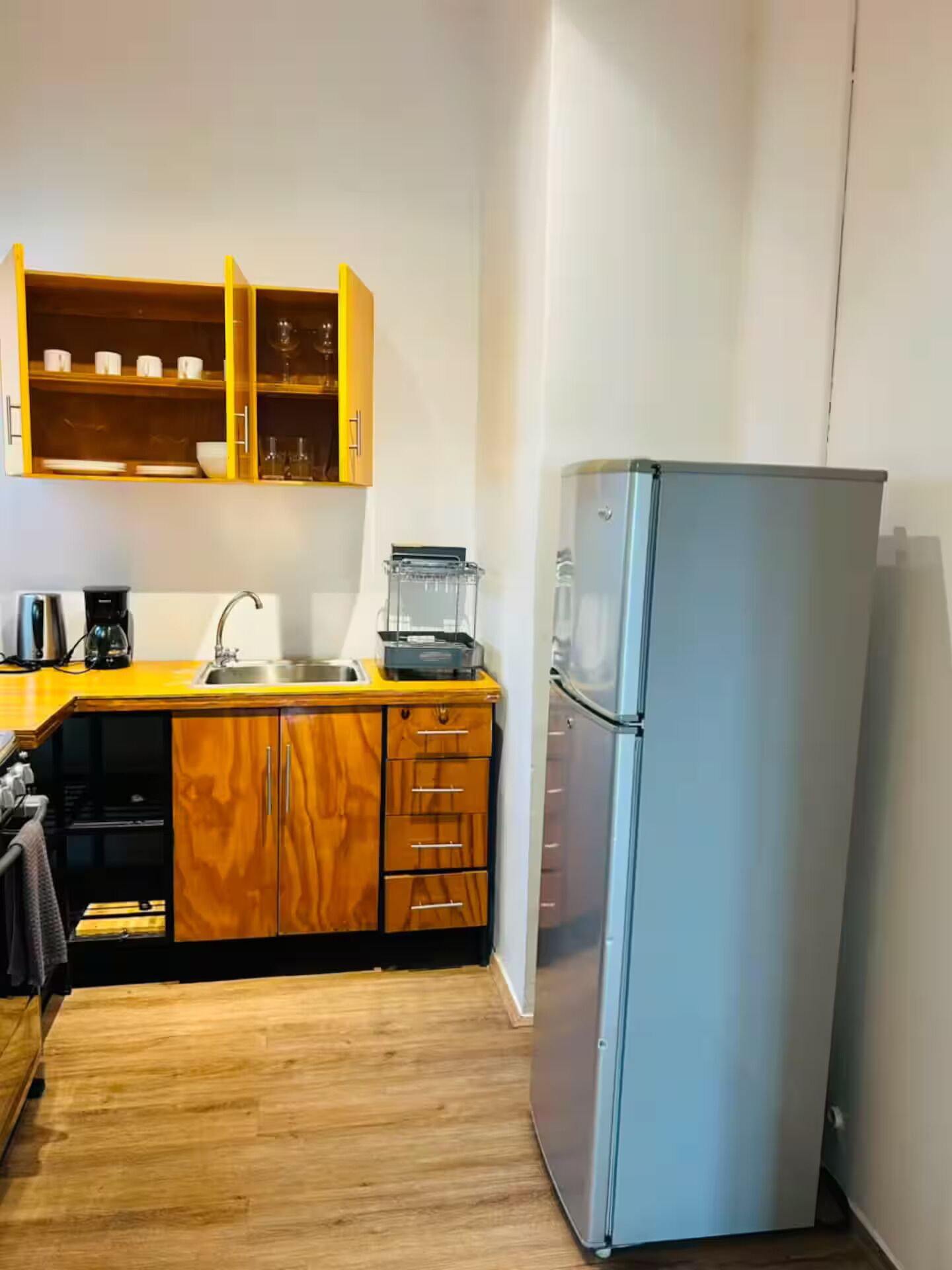 Una cocina compacta con armarios de madera, un lavamanos de acero inoxidable y un refrigerador empotrado.