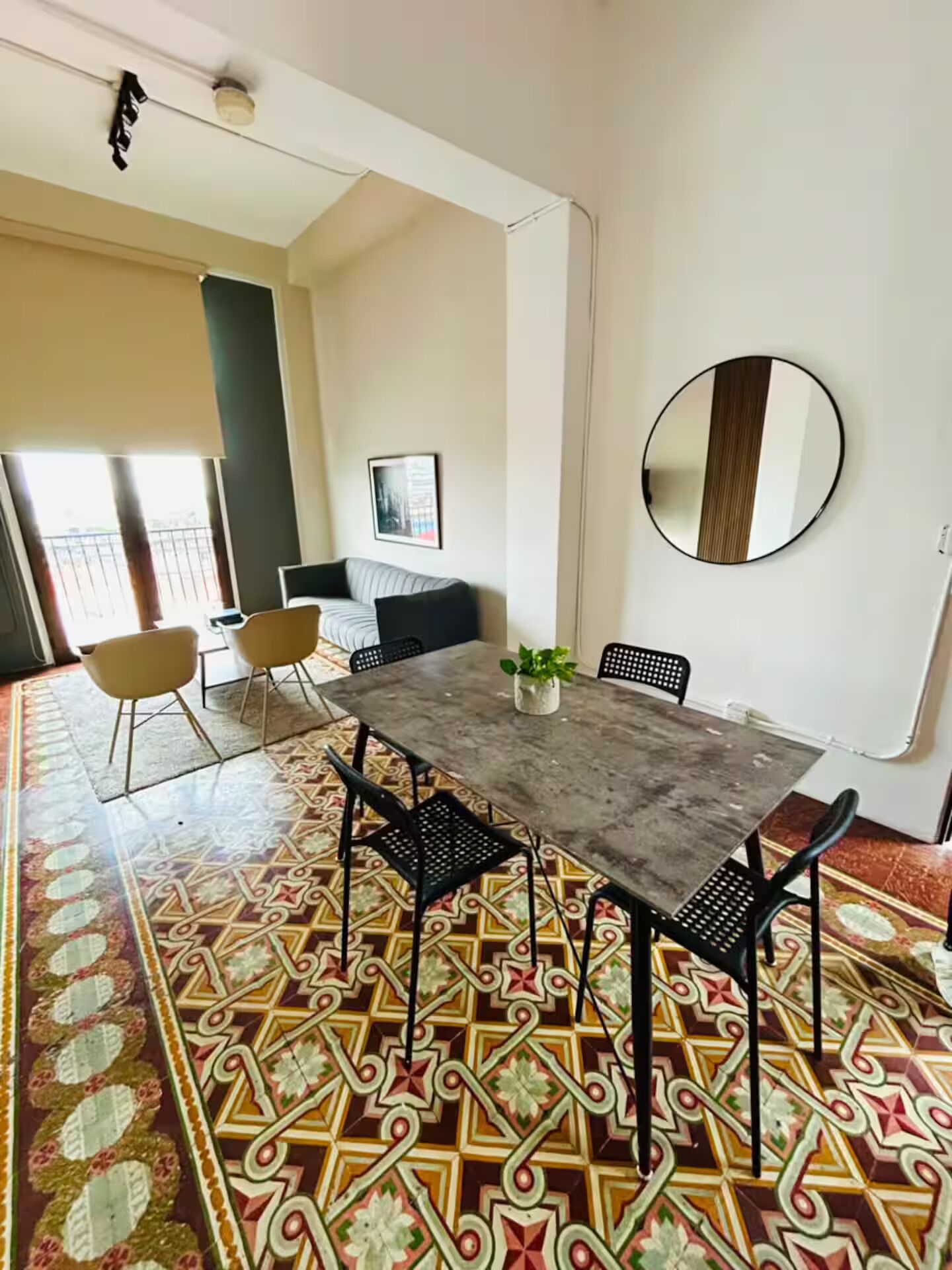 A dining area with a table, chairs, a potted plant, and a round mirror on the wall.