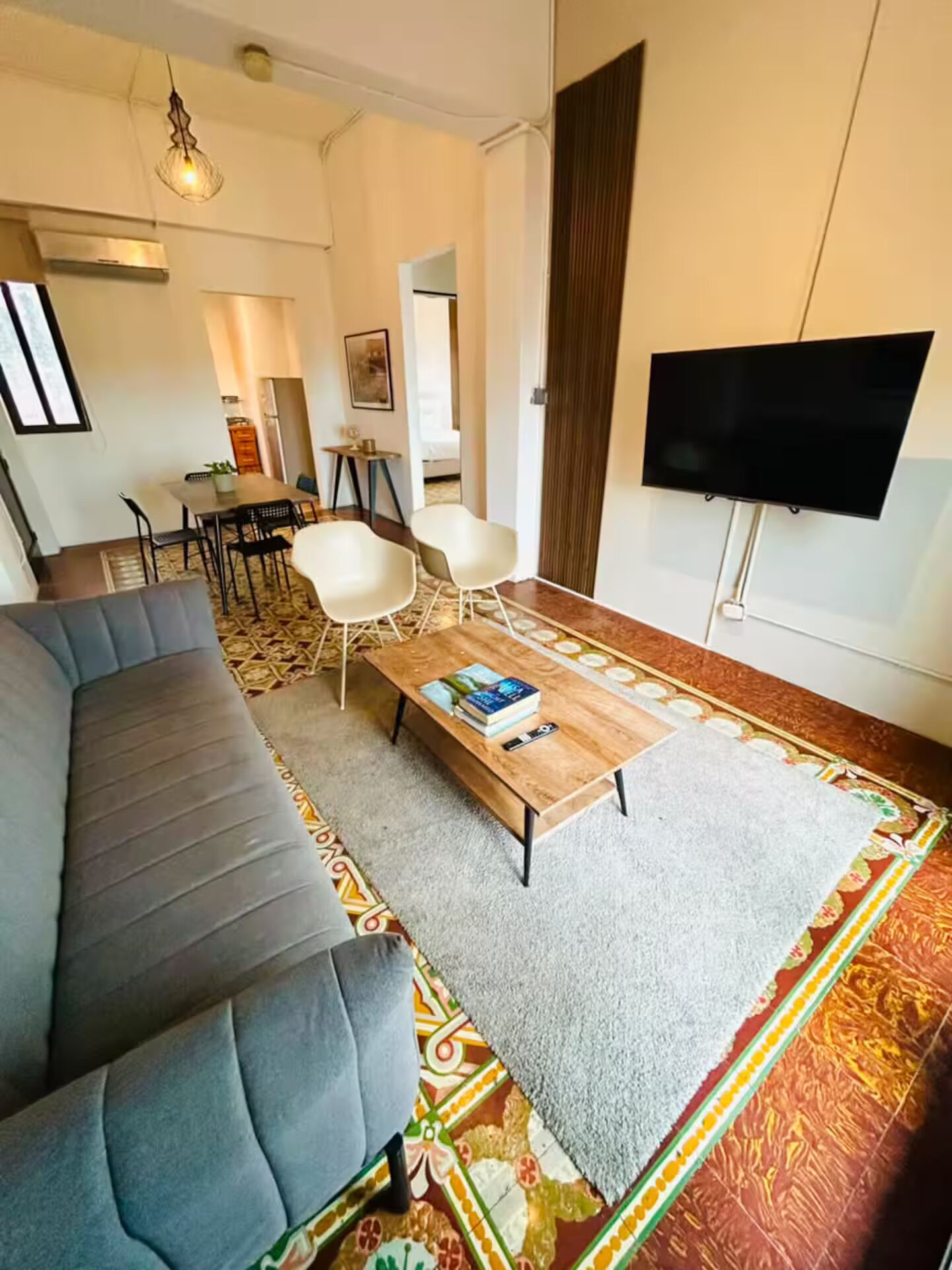 A modern living room with a grey sofa, a coffee table with books, a flat-screen TV, and a patterned rug.