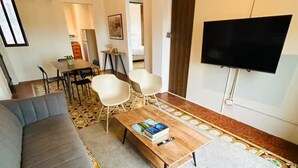 A modern living room with a grey sofa, a coffee table with books, a flat-screen TV, and a patterned rug.