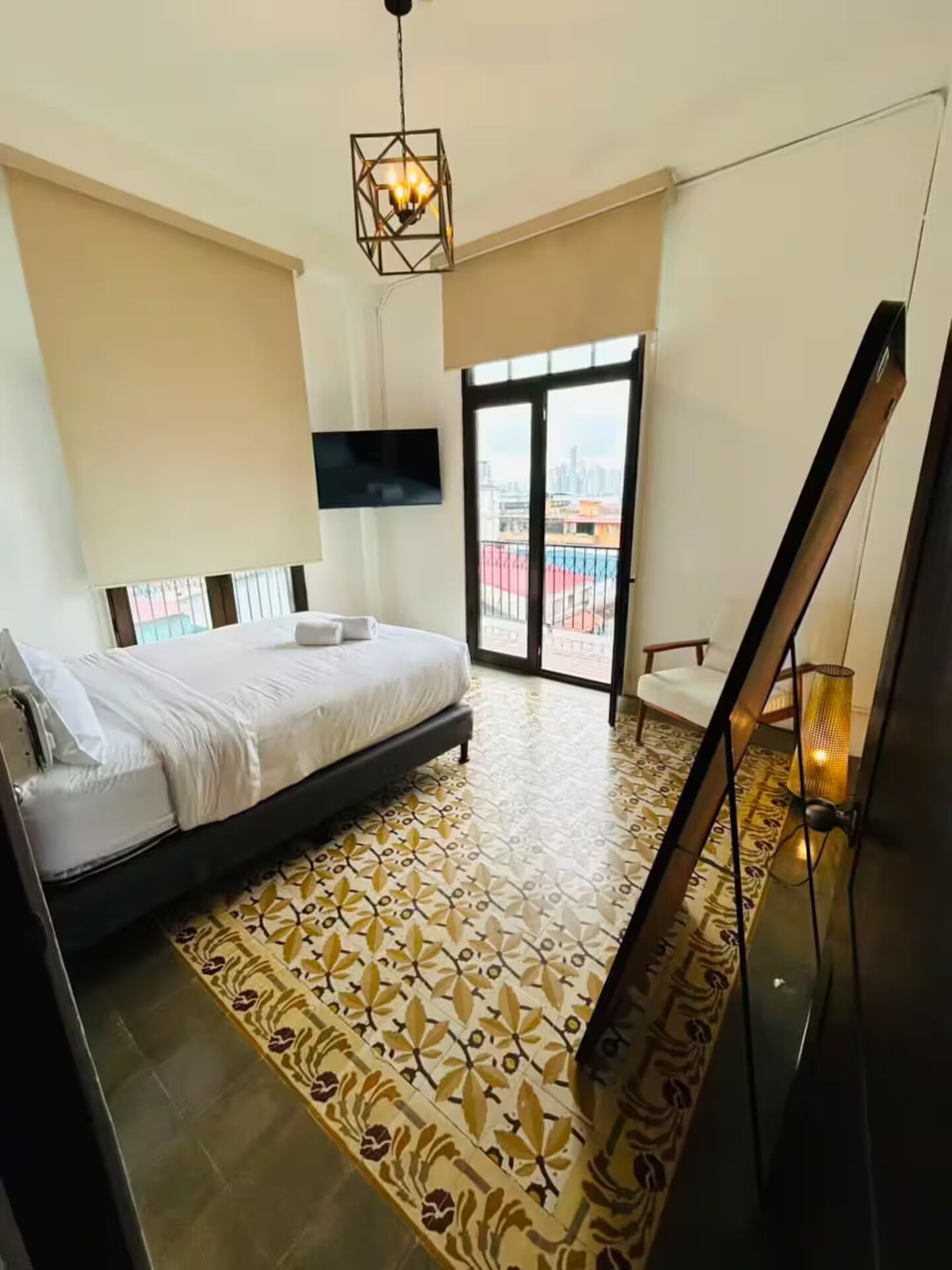 A hotel room with a bed, a TV, a balcony with a view, and a patterned floor.