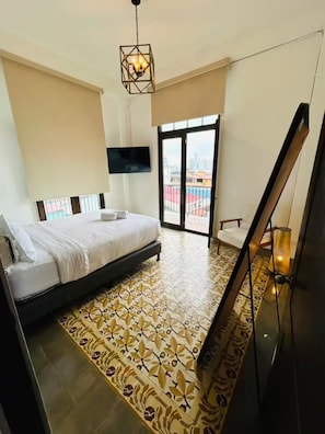 A hotel room with a bed, a TV, a balcony with a view, and a patterned floor. - La Botica, Casa Donovan (Panamá)