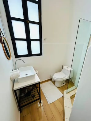 A compact bathroom with a white sink, toilet, and a small window with blinds. - La Botica, Casa Donovan (Panamá)