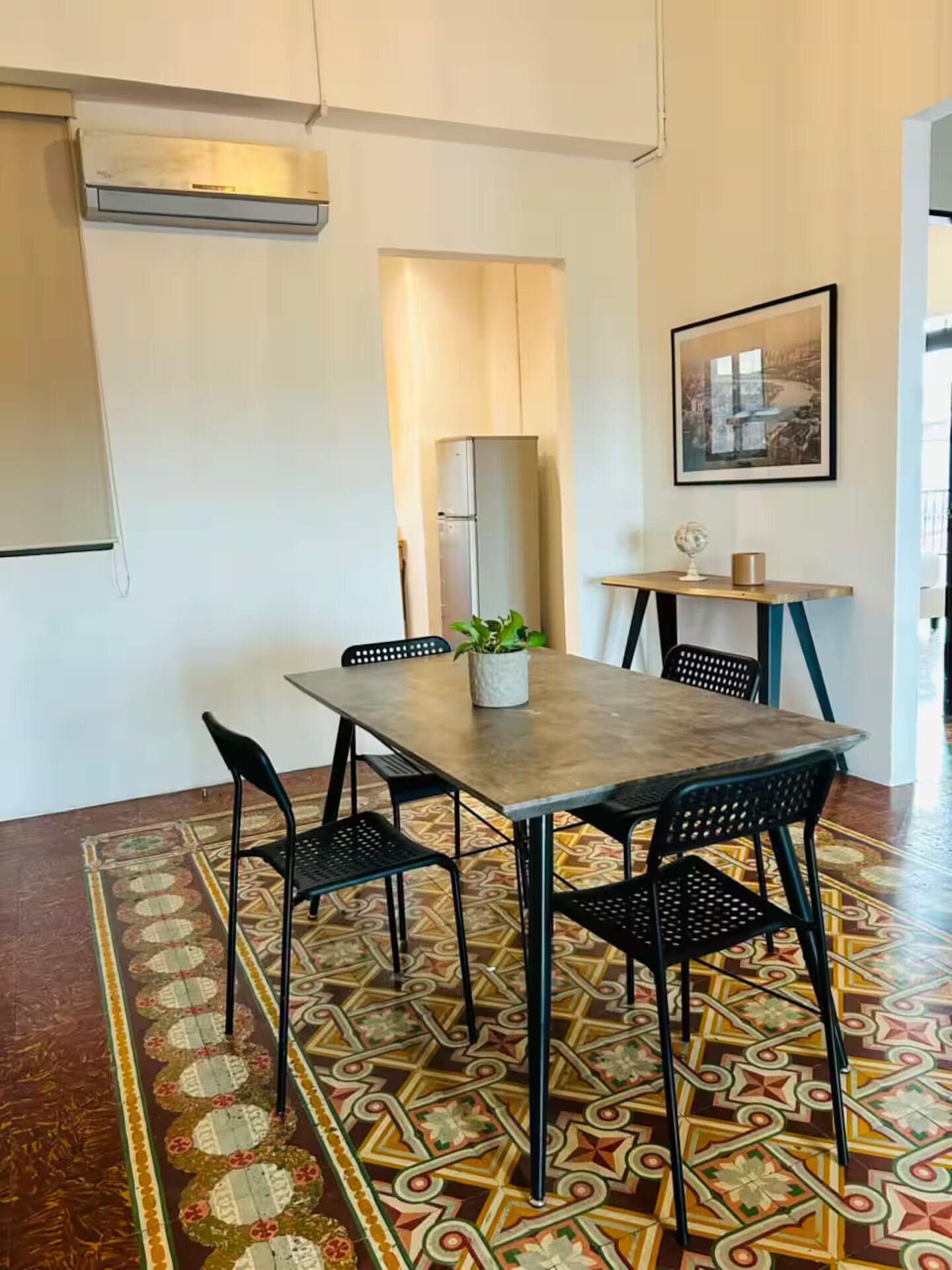A dining area with a table, chairs, a potted plant, and a patterned floor.