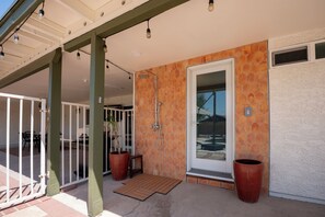 A covered patio area with a shower, potted plants, and a door leading to a room. - Modern Mesa Retreat Pool Near Gilbert & US-60 (Mesa)