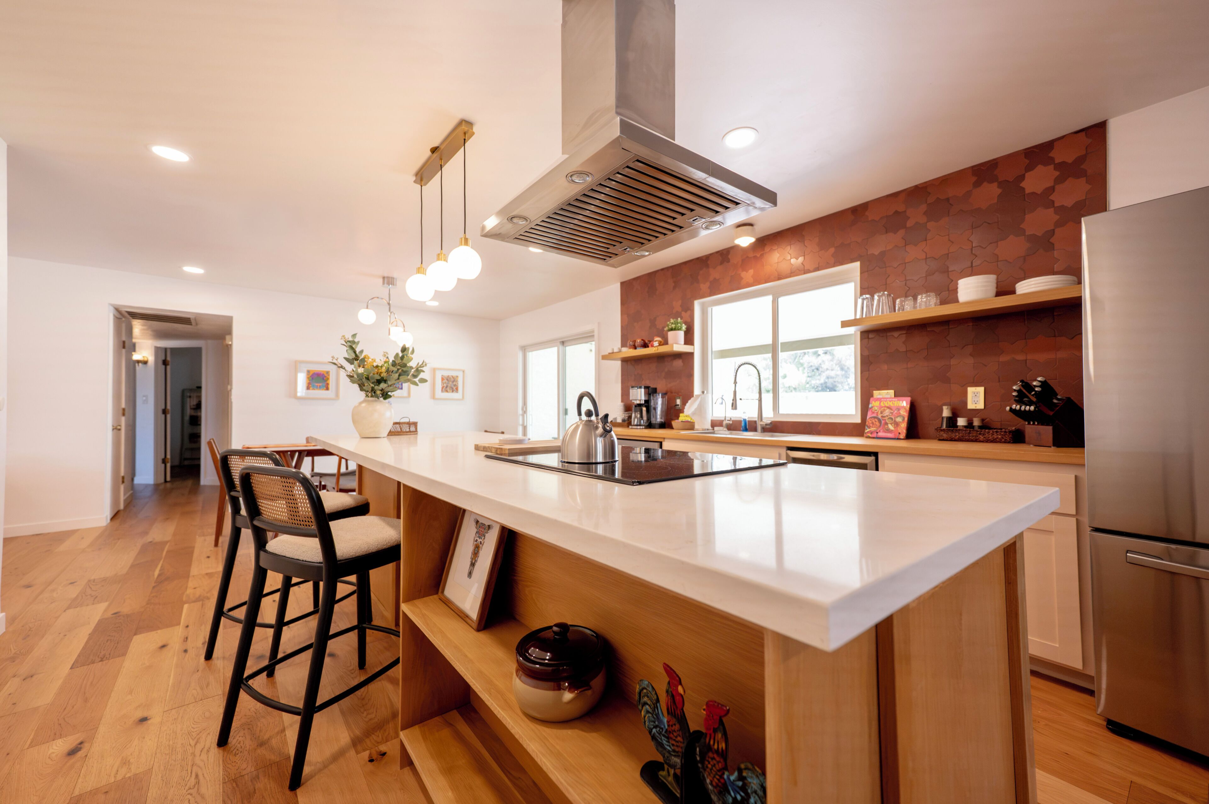 A modern kitchen with a central island, bar stools, a stainless steel refrigerator, and a window providing natural light.
