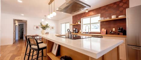Una cocina moderna con una isla central, taburetes de bar, un refrigerador de acero inoxidable y un ventanal que proporciona luz natural.