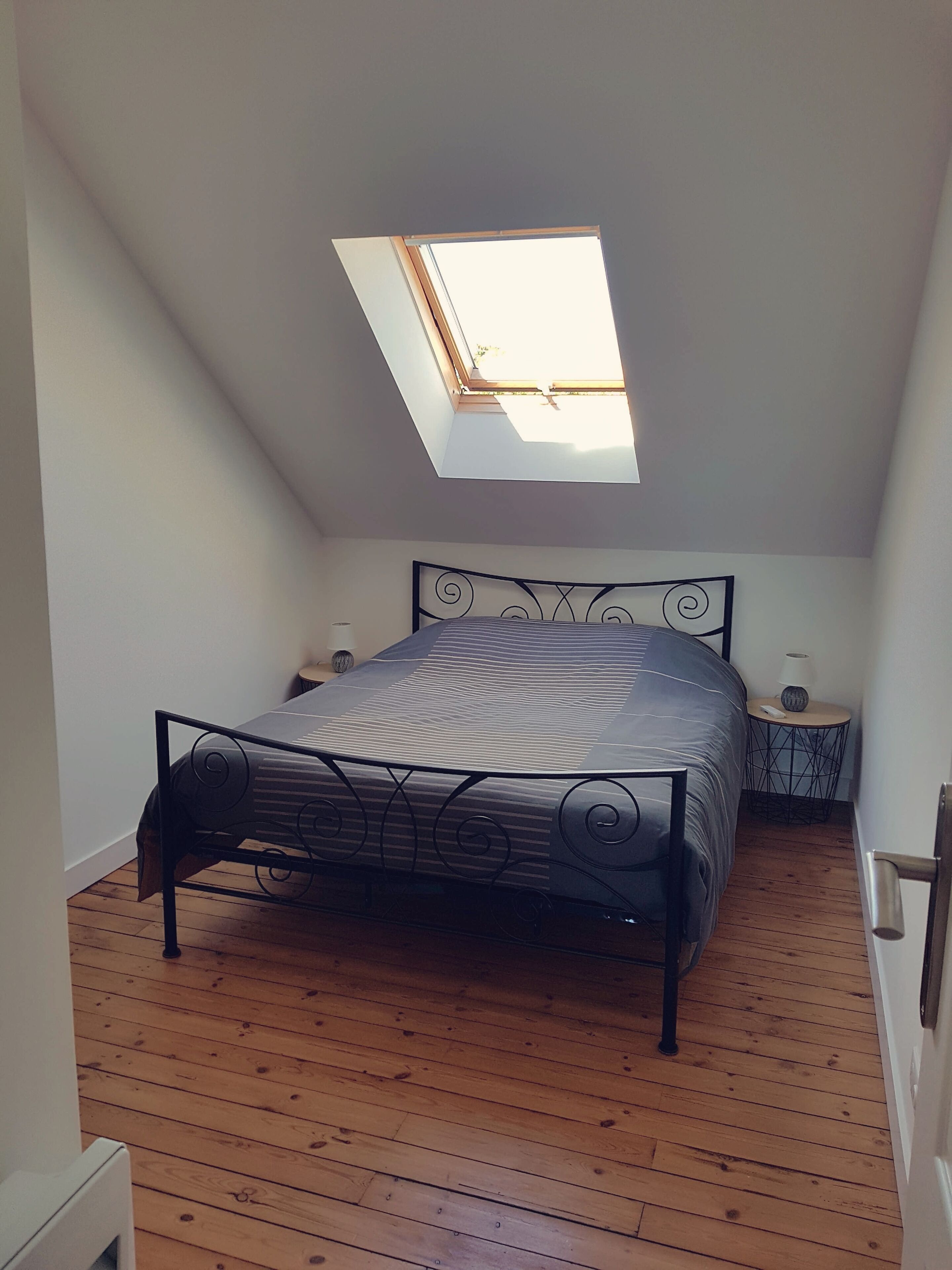 A bedroom with a sloped ceiling, a bed with a metal frame, a small bedside table, and a skylight.