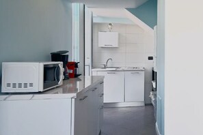 Een kleine keuken met witte kastjes, een magnetron en een spoelbak.