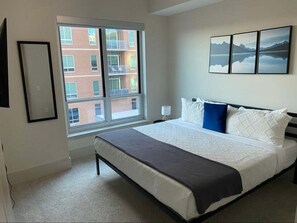 A bedroom with a large window, a bed with white bedding, a black headboard, and a wall-mounted picture. - Preston Royal Double II I Premium 2BR in Dallas (Dallas)