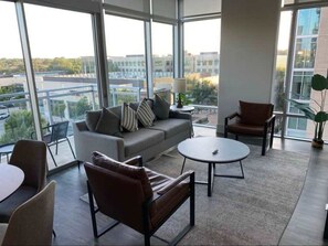 Un salon moderne comprenant un canapé, des fauteuils et une table basse, avec de grandes fenêtres offrant une vue sur la ville.