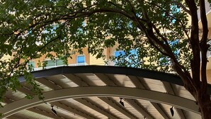 An outdoor patio area with a covered seating area, a barbecue grill, and a pool in the background. - Preston Royal Double II I Premium 2BR in Dallas (Dallas)