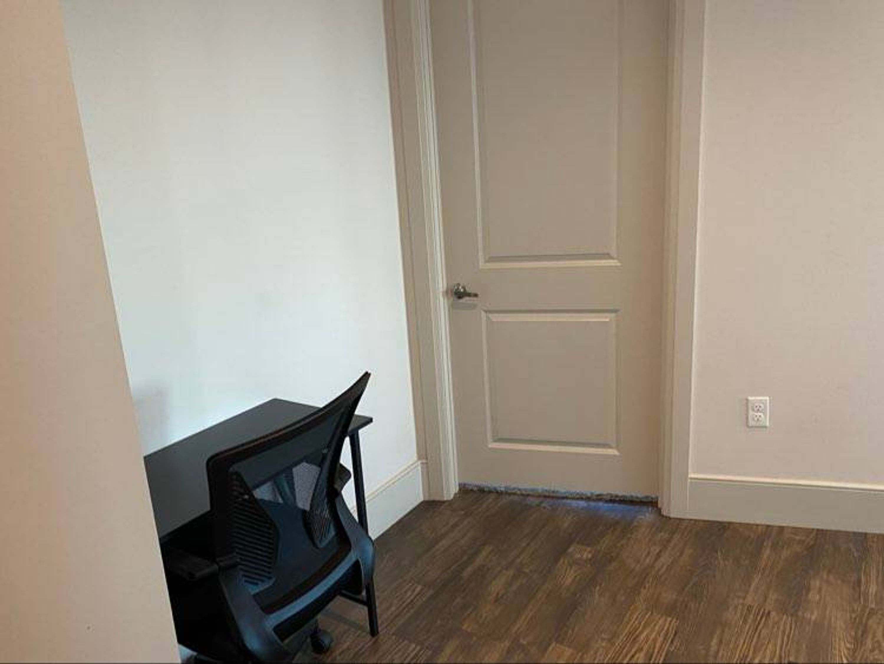 A room with a closed door, a black office chair, and a wooden floor.