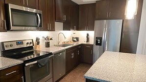 A modern kitchen with stainless steel appliances, dark wood cabinets, and a granite countertop. - Preston Royal Single II I Premium 1BR in Dallas (Dallas)