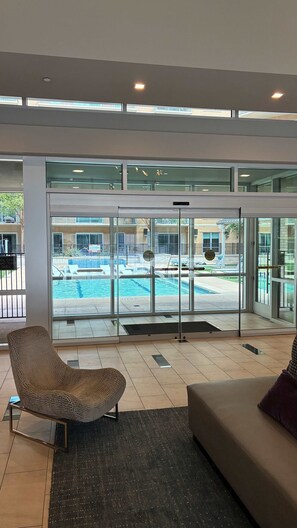 A modern hotel lobby with a glass door leading to a pool area, a lounge chair, and a sofa. - Preston Royal Single II I Premium 1BR in Dallas (Dallas)