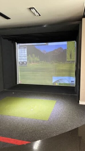 A room with a large screen displaying a landscape, a green mat on the floor, and a red line marking a boundary. - Preston Royal Single II I Premium 1BR in Dallas (Dallas)