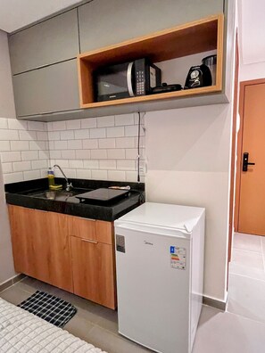 Una cocina compacta con microondas, un refrigerador pequeño y un estante de madera sobre la encimera.