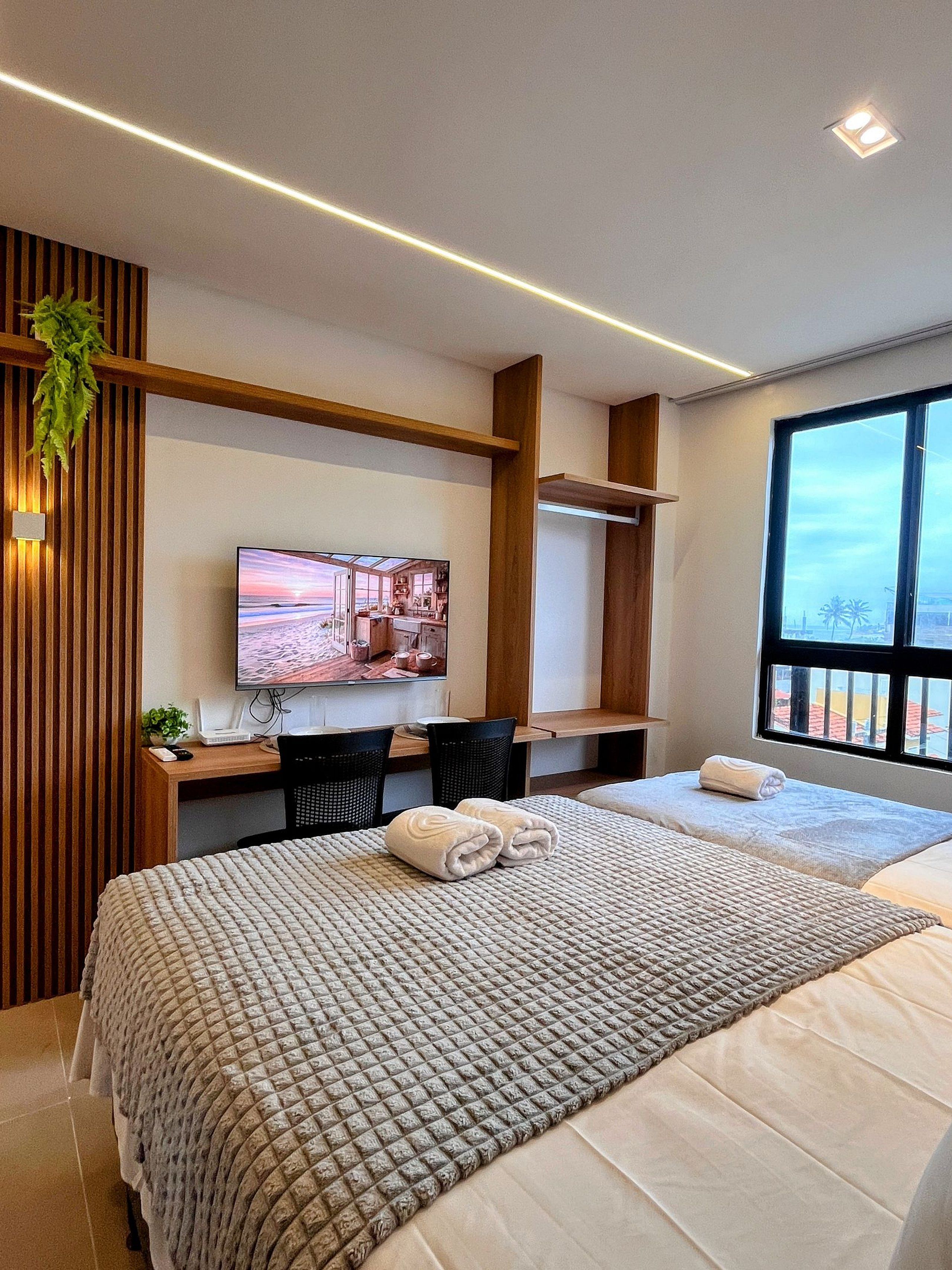 Une chambre d’hôtel moderne dotée d’un grand lit, d’un bureau avec un ordinateur, d’une télévision et d’une fenêtre offrant une vue agréable.