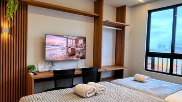 Una habitación de hotel moderna con una cama grande, un escritorio con computadora, un televisor y una ventana con vistas.