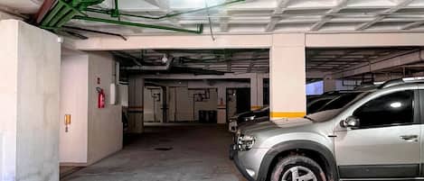 A parking garage with concrete pillars, a silver car parked, and visible fire extinguishers.