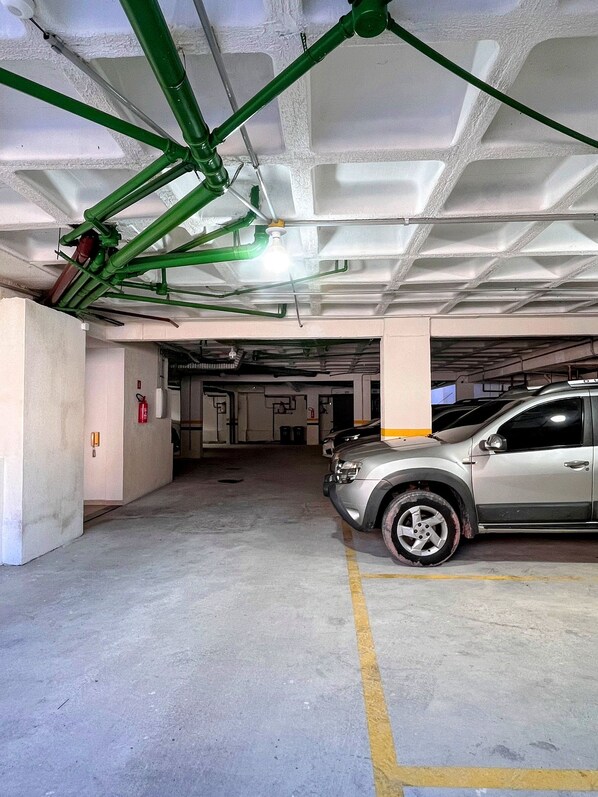 A parking garage with concrete pillars, a silver car parked, and visible fire extinguishers.